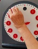 Main réglant les aiguilles d’une horloge pédagogique, atelier Montessori seniors